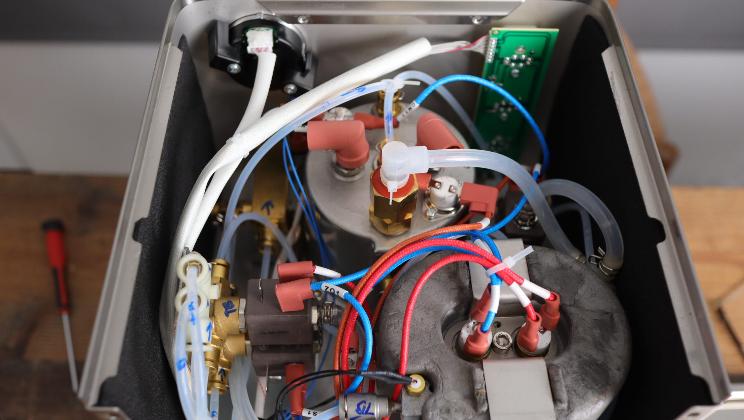 View of the inside of the MiiCoffee Apex, with the stainless steel brew boiler in the background, water circuits on the left, and thermoblock in the foreground